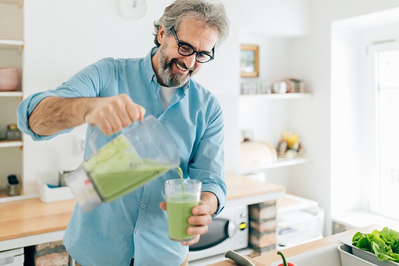 man pouring a green smoothie into a glass