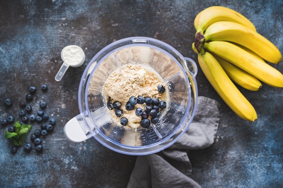 blender with protein powder and berries and a bunch of bananas