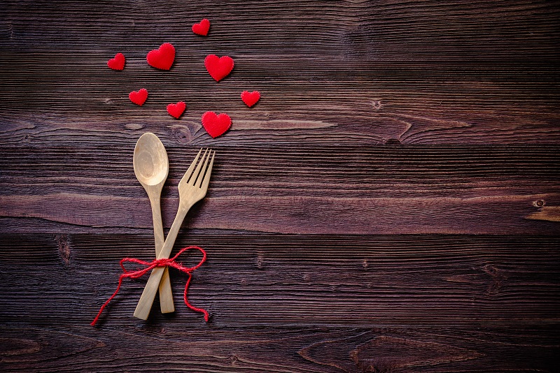 wooden spoon and fork tied with red ribbon on a table with cut-out red hearts