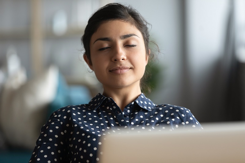 smiling woman sitting at her computer with her eyes closed