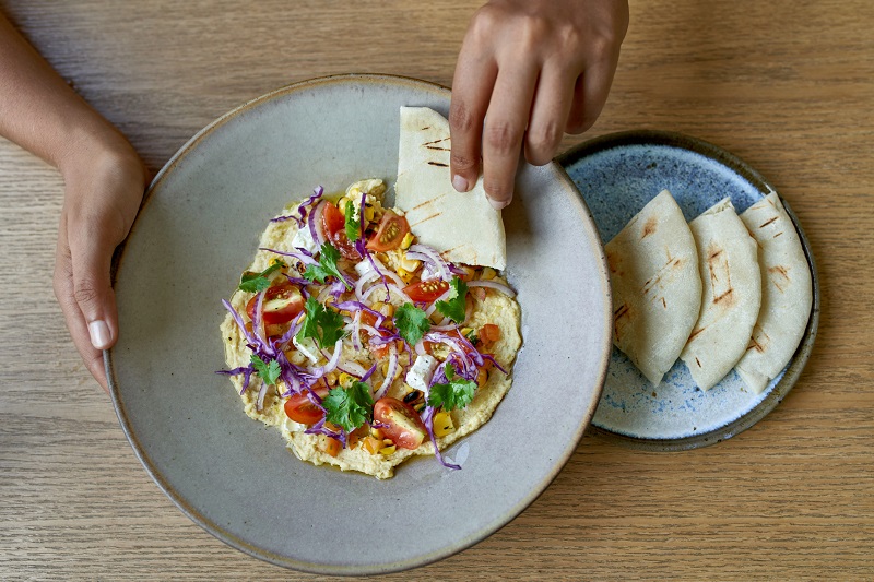 person dipping naan into a bowl of hummus