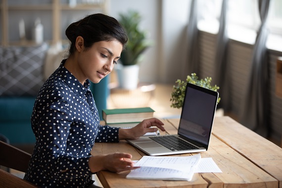 woman looking at notepad while typing on laptop