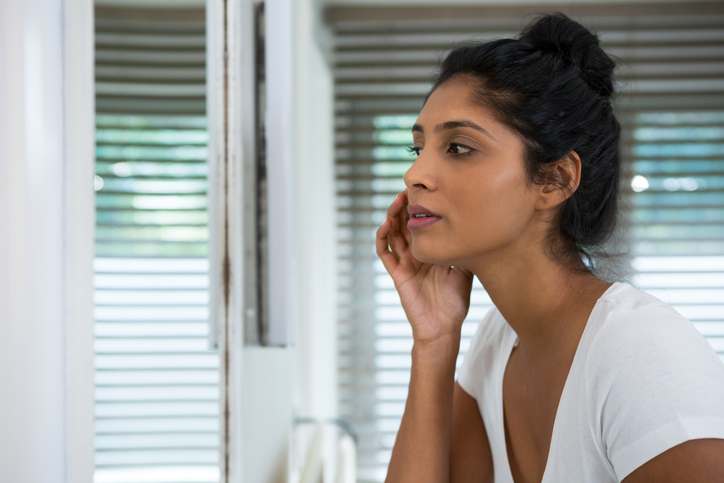 Woman checking her pimple in the mirror.